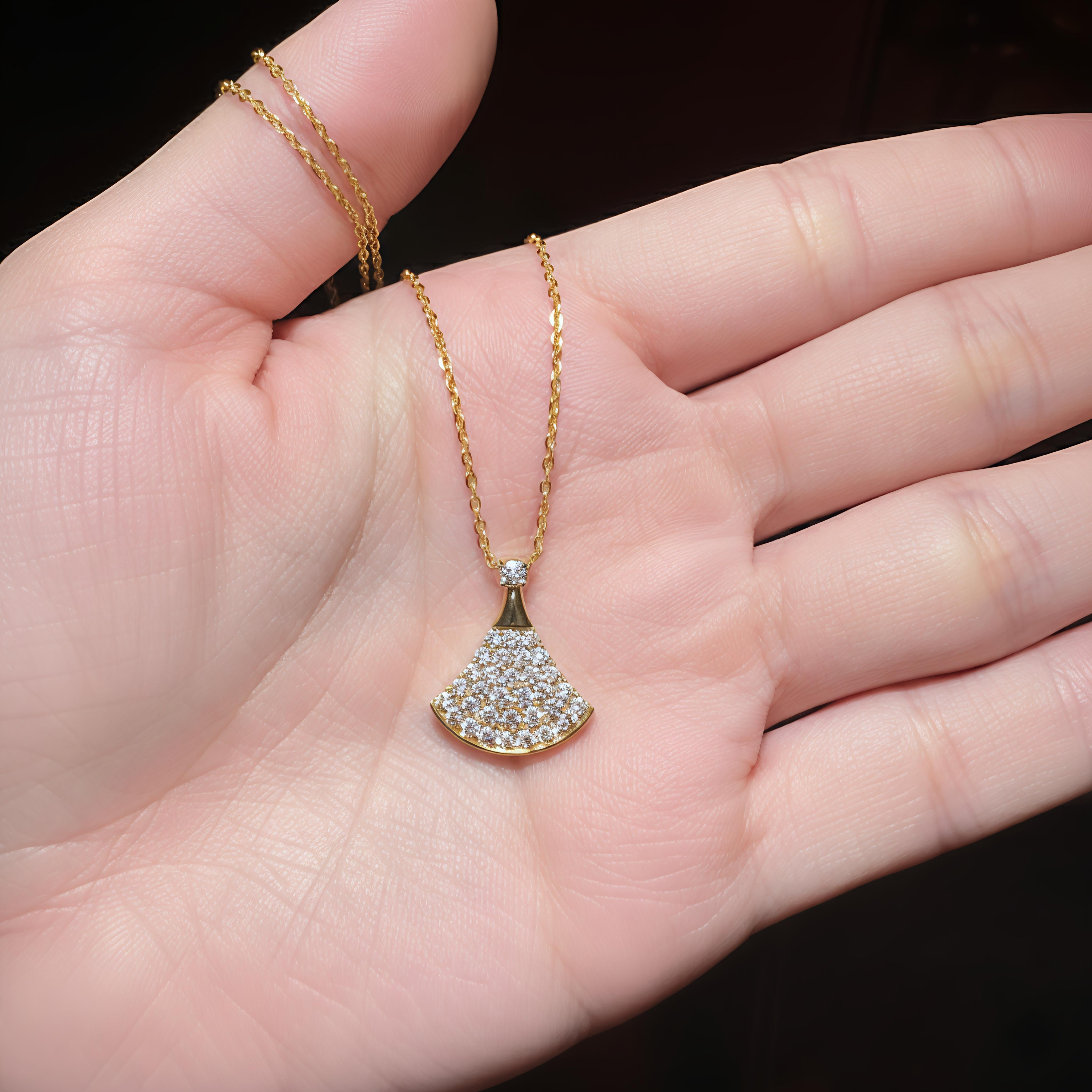 Gold necklace with a fan-shaped pendant held in a hand against a dark background