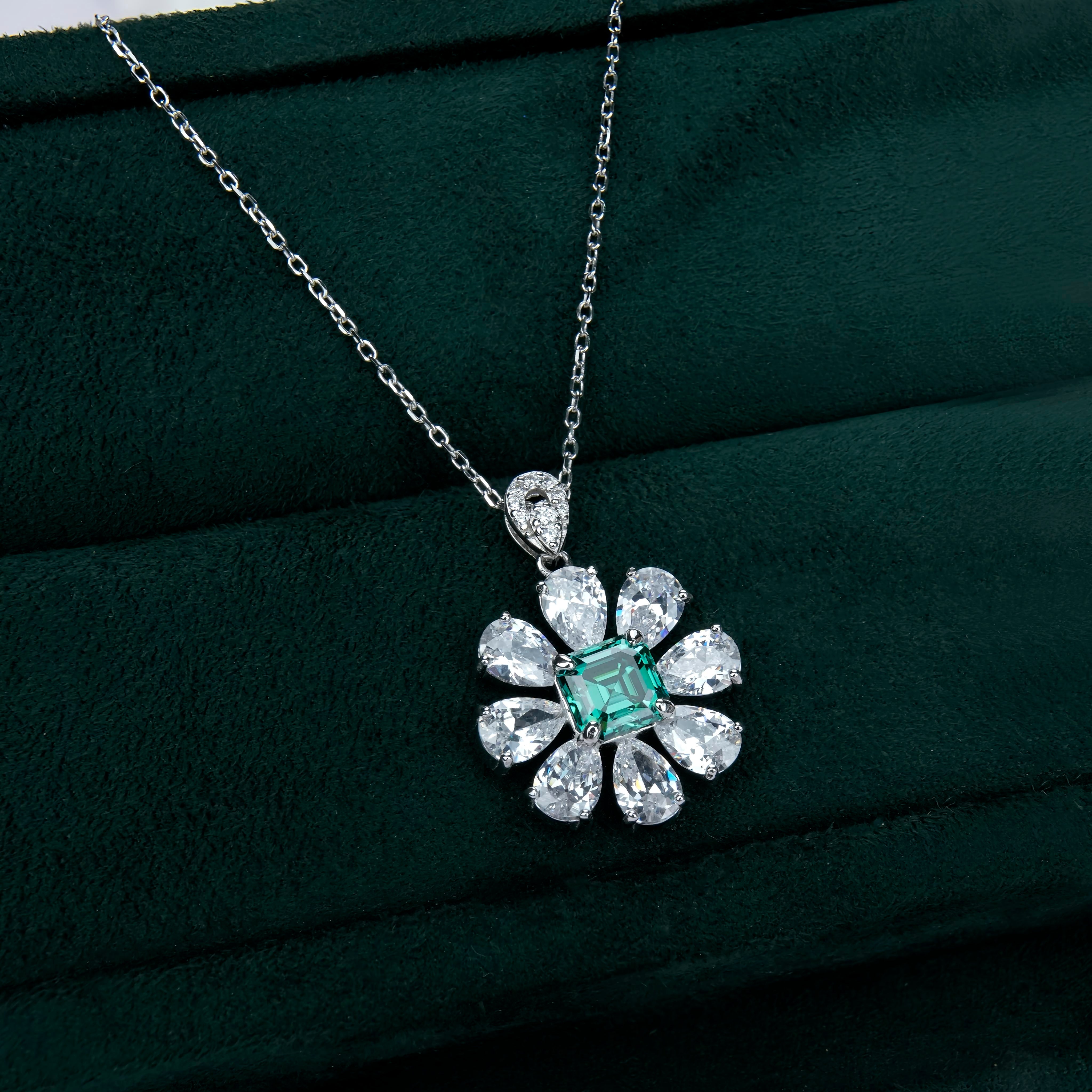 Silver necklace with a flower-shaped pendant featuring a green gemstone on a dark green background