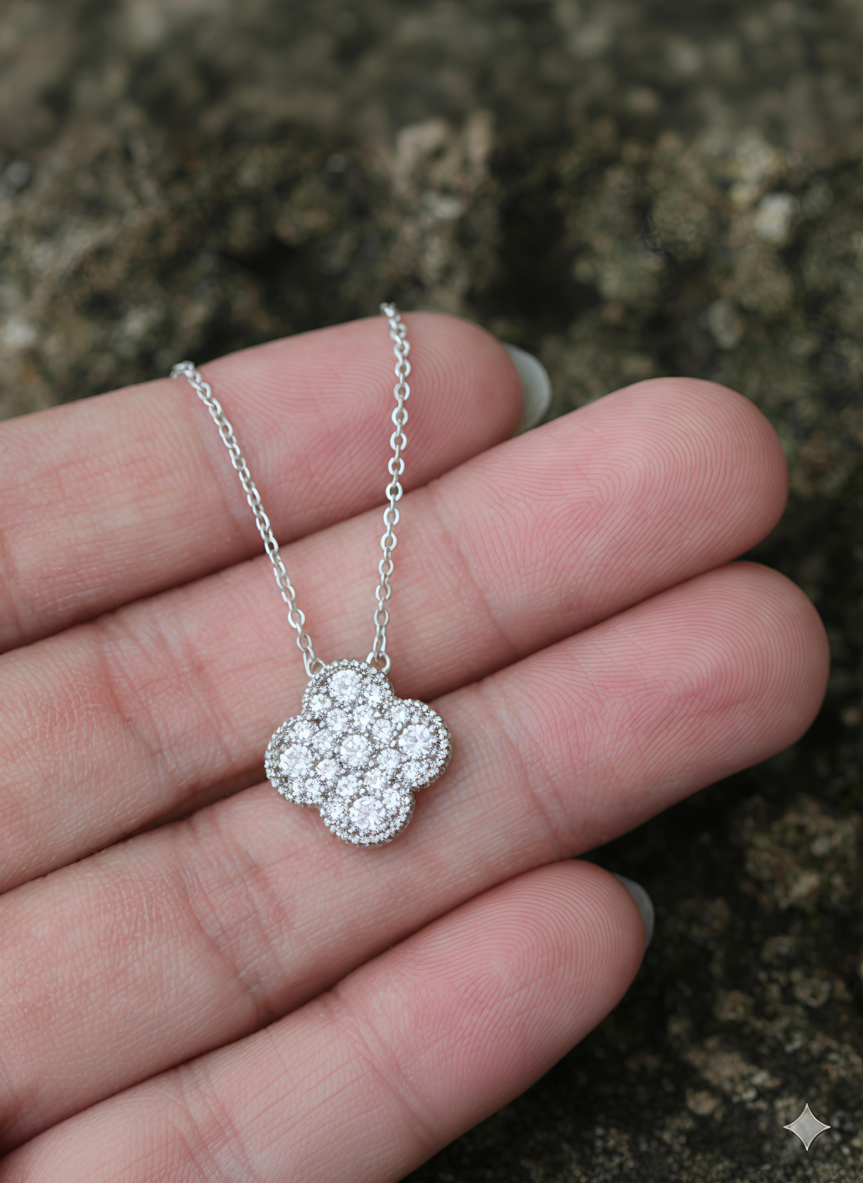 Silver necklace with a floral pendant held in a hand against a textured background