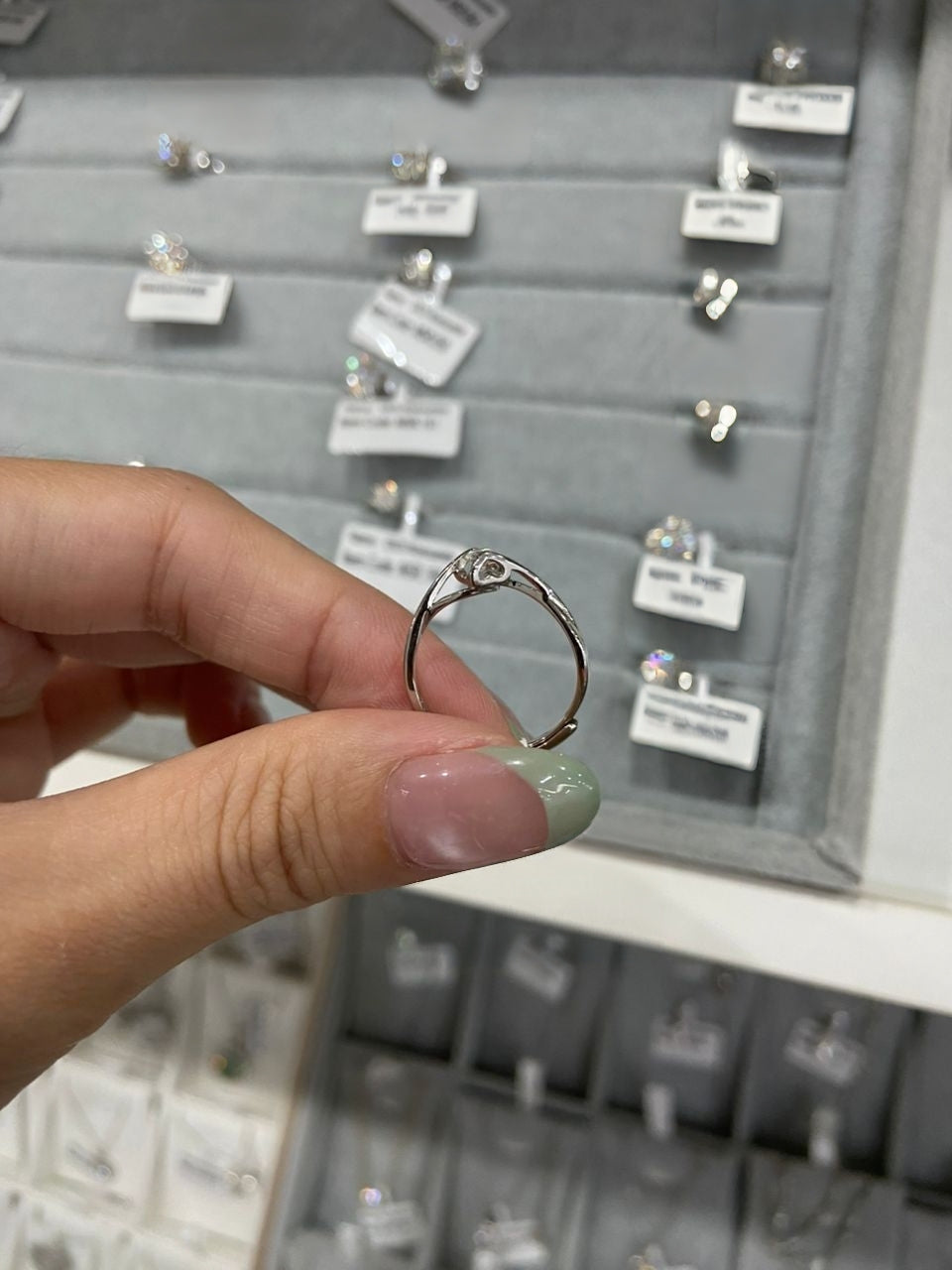 Hand holding a silver ring with a display of other rings in the background