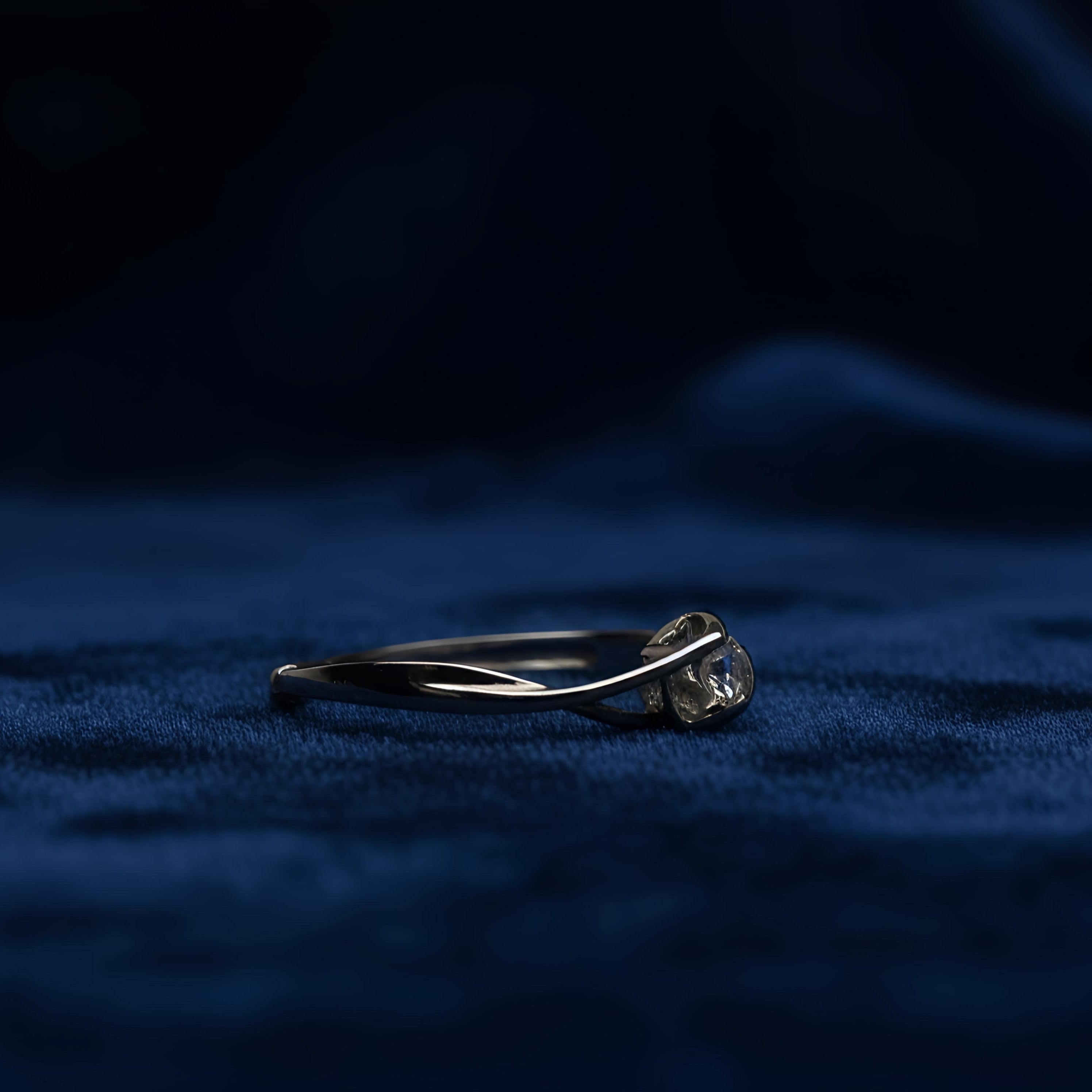 Silver ring with a diamond on a dark blue fabric background