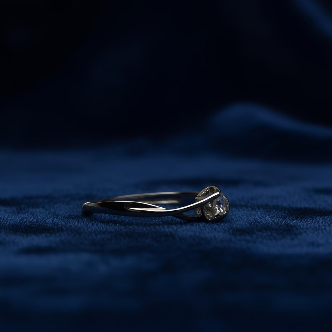 Silver ring with a diamond on a dark blue fabric background