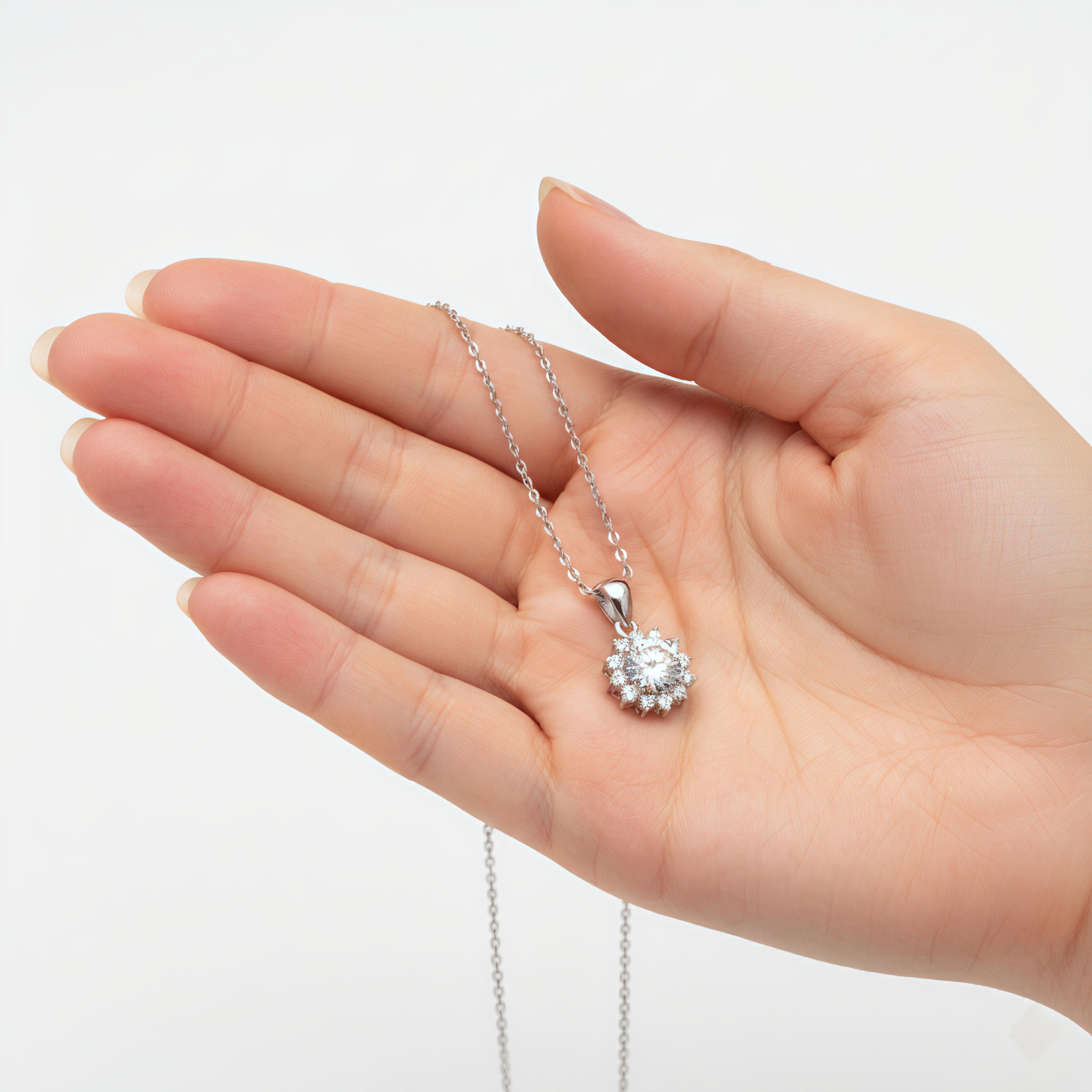 Hand holding a silver necklace with a diamond pendant against a white background
