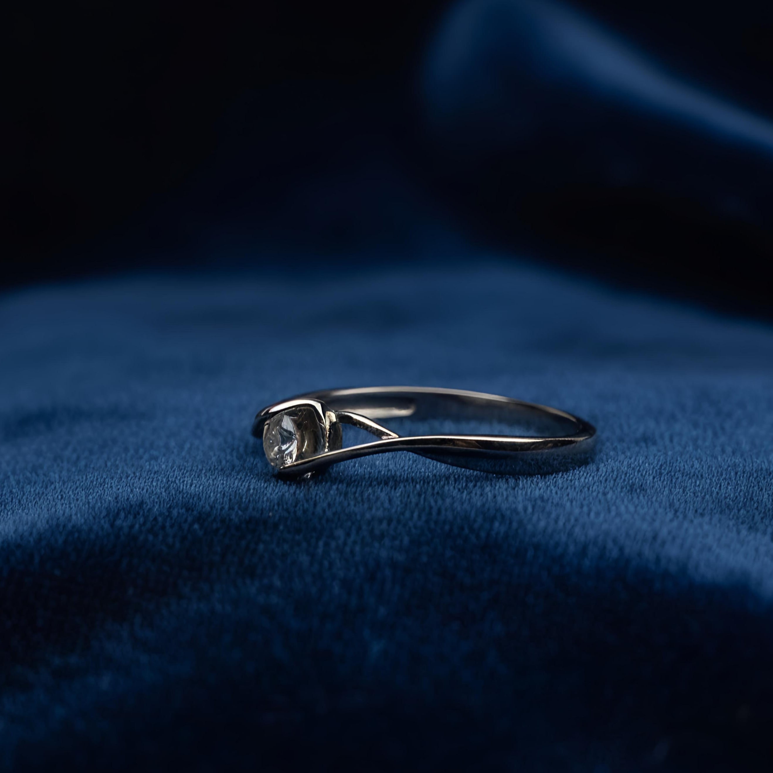 Silver ring with a diamond on a blue fabric background